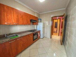 A kitchen with wooden cabinets, a gas stove, a refrigerator, and a tiled floor.