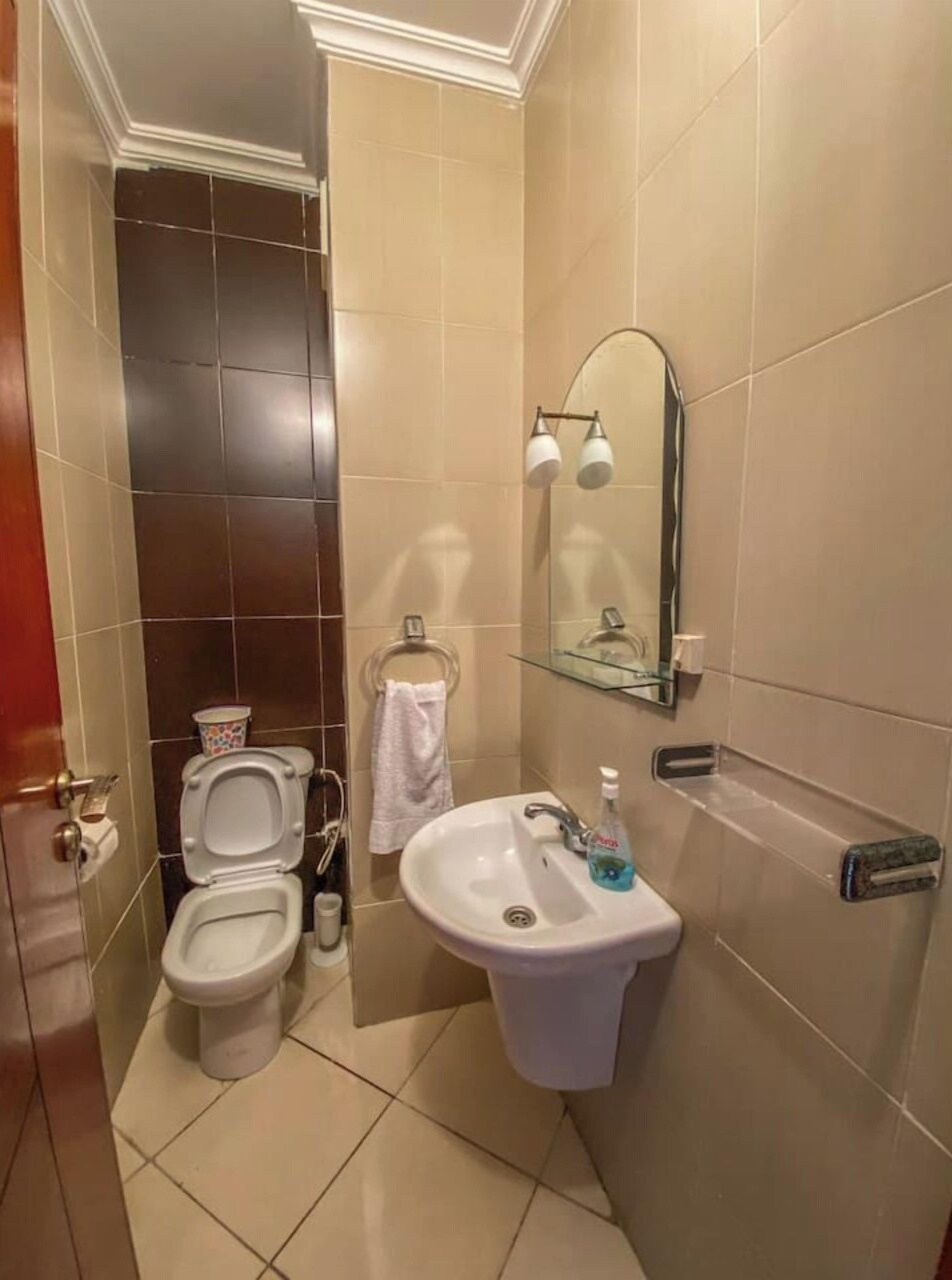 A bathroom with two toilets, a sink, a mirror, and a glass shelf.
