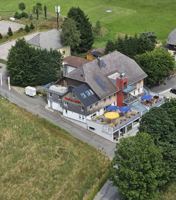 A two-story building with a flat roof, a visible chimney, and a ground-level outdoor seating area with umbrellas. - Hotel Lafette (Titisee-Neustadt)