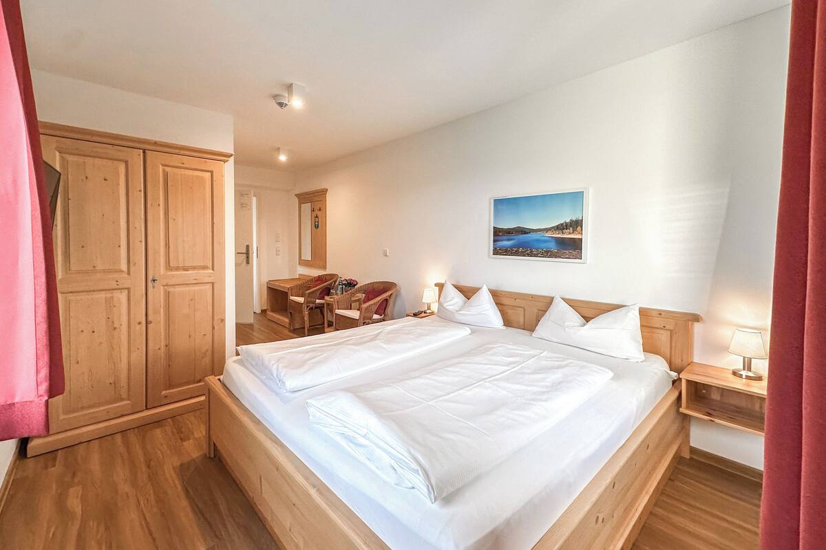 A bedroom with a large bed, wooden wardrobe, and a desk with chairs.