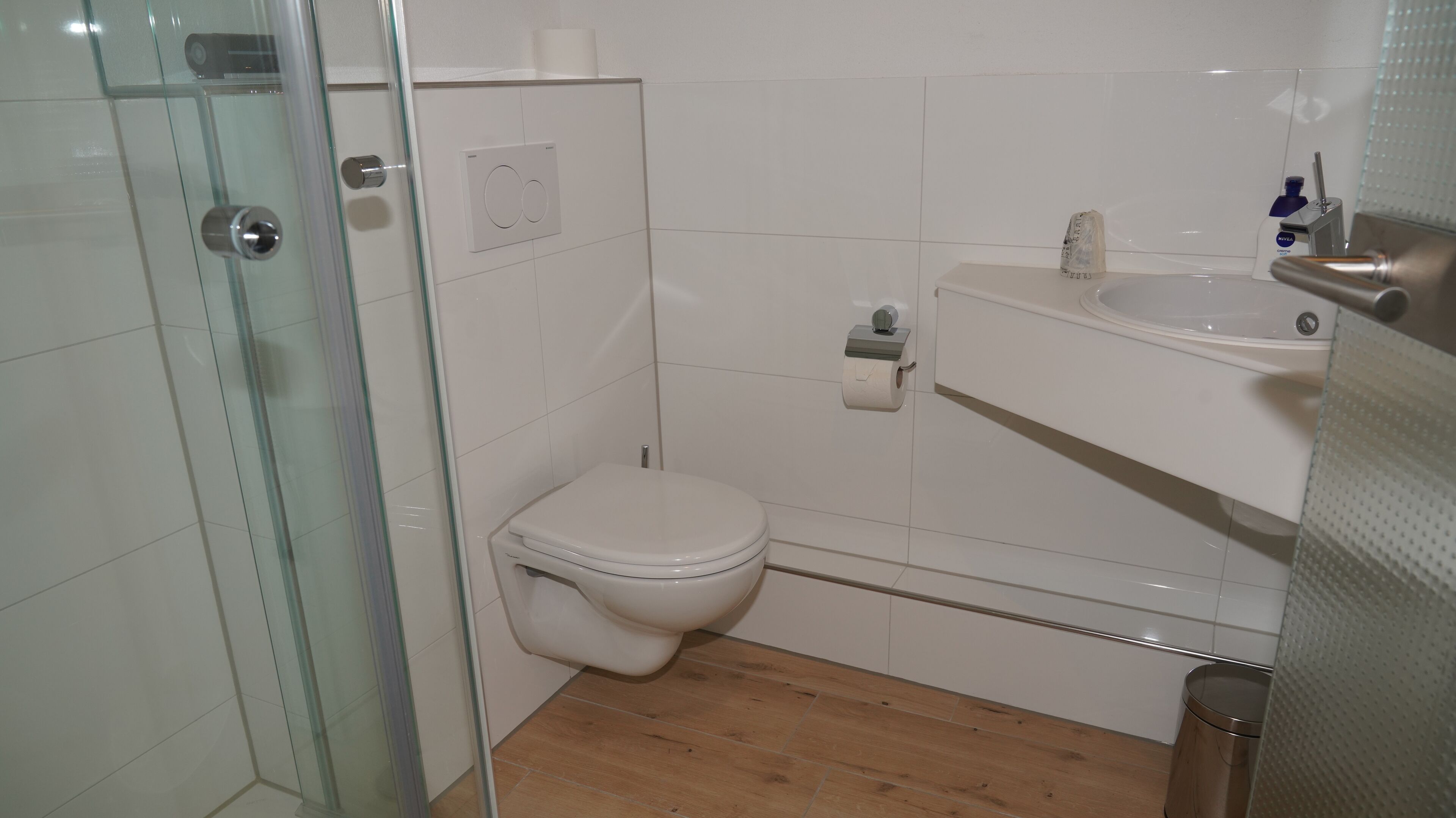 A small, modern bathroom with a glass shower enclosure, a toilet, and a sink with a mirror.