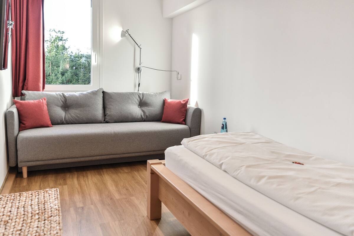 A modern bedroom with a grey sofa, a wooden bench, and a bed with white bedding.