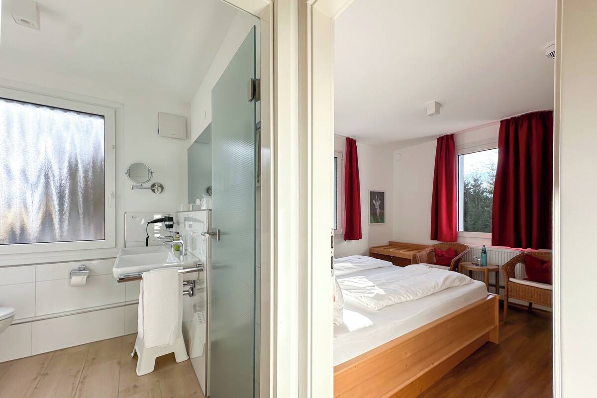 A modern bedroom with a wooden bed, a small bedside table, and a window with red curtains.
