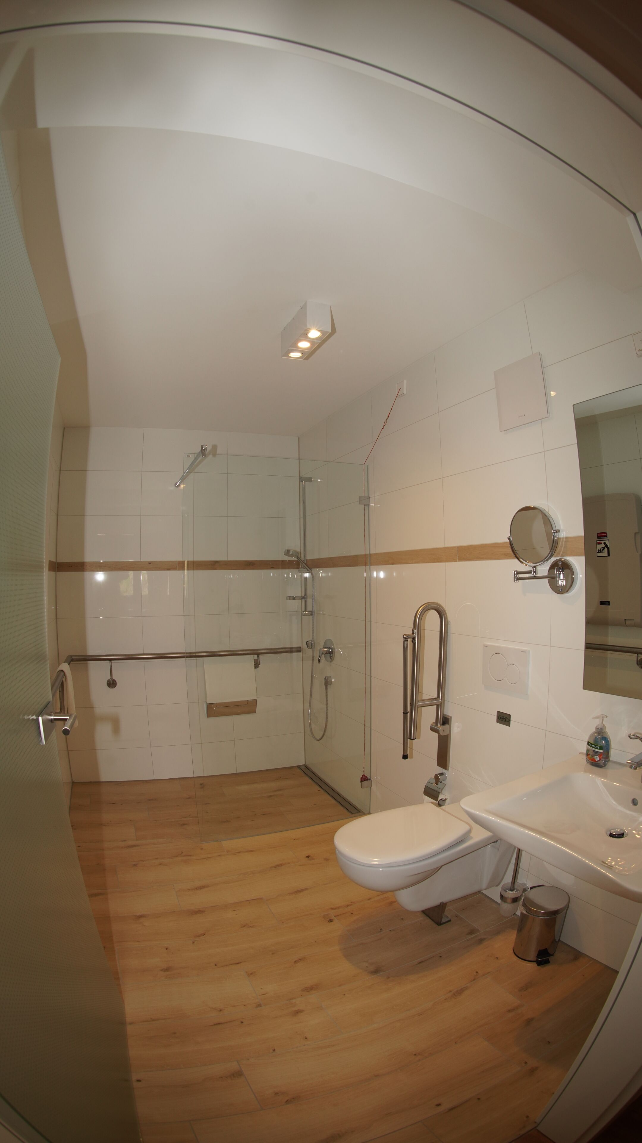 Un baño moderno con cabina de ducha de vidrio, piso de madera, lavamanos blanco y espejo.