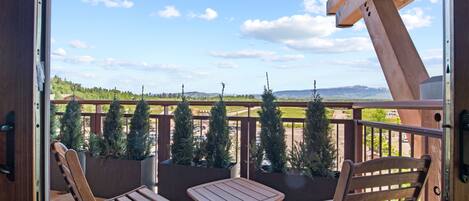 Een balkon met houten stoelen en een tafel, met uitzicht op een aangelegd gebied met bomen en heuvels in de verte.