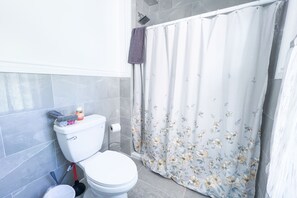 A bathroom with a toilet, shower curtain, and tiled walls. - The Haines Villa (Niagara Falls)