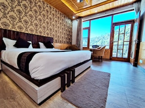 Ein großes Bett mit Holz-Kopfteil, ein Schreibtisch und ein Blick ins Freie durch ein großes Fenster.