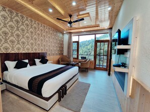 A bedroom with a large bed, a ceiling fan, a TV mounted on the wall, and a view of the outdoors. - Nature Villa Resort (Kandaghat)