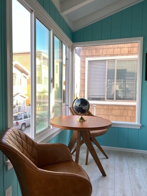 Una habitación con paredes color turquesa, una mesa de madera con un globo terráqueo, un sillón de cuero y ventanas amplias con vistas a la calle.