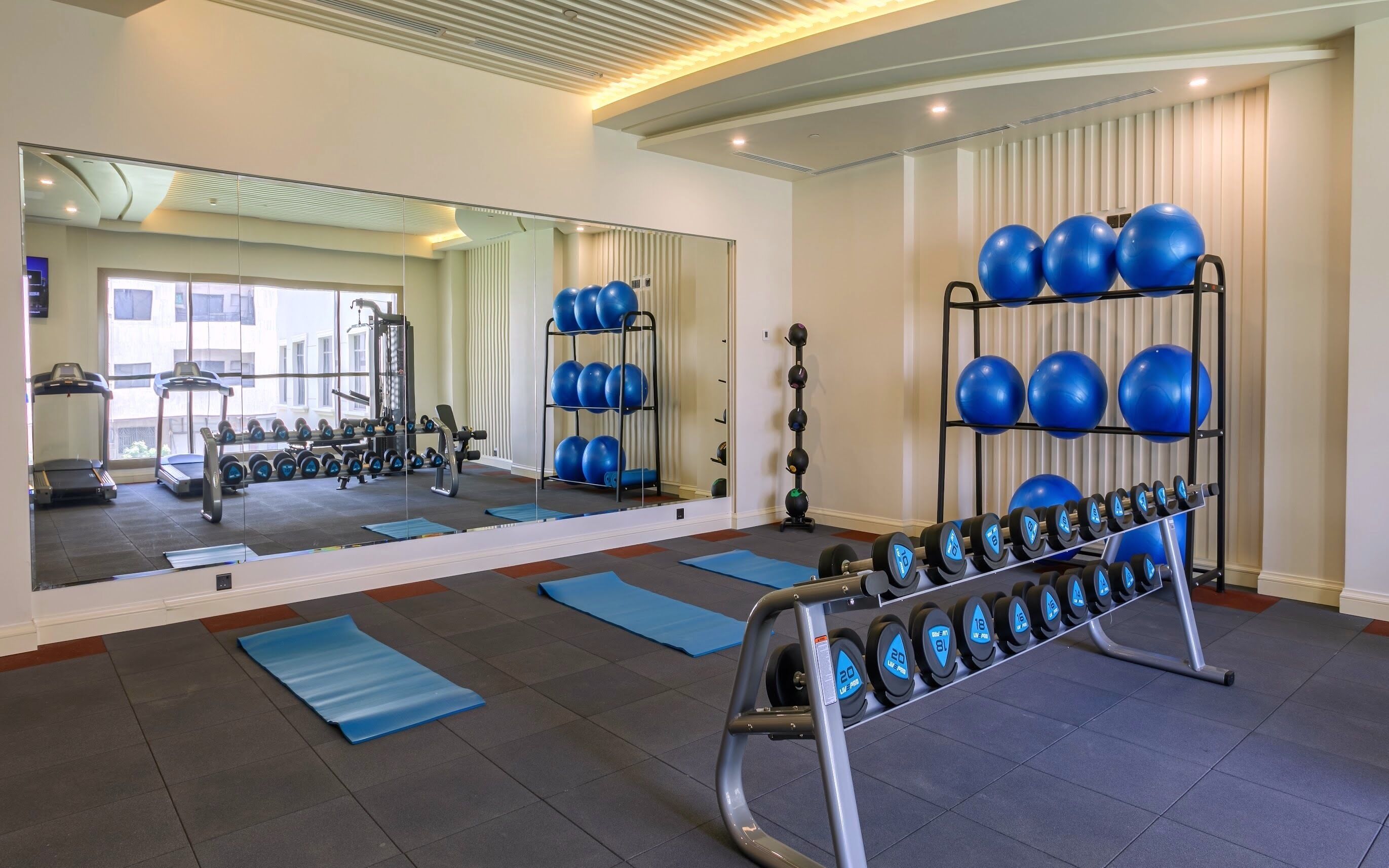 Un gimnasio con equipo de ejercicio, colchonetas azules y un espejo grande.