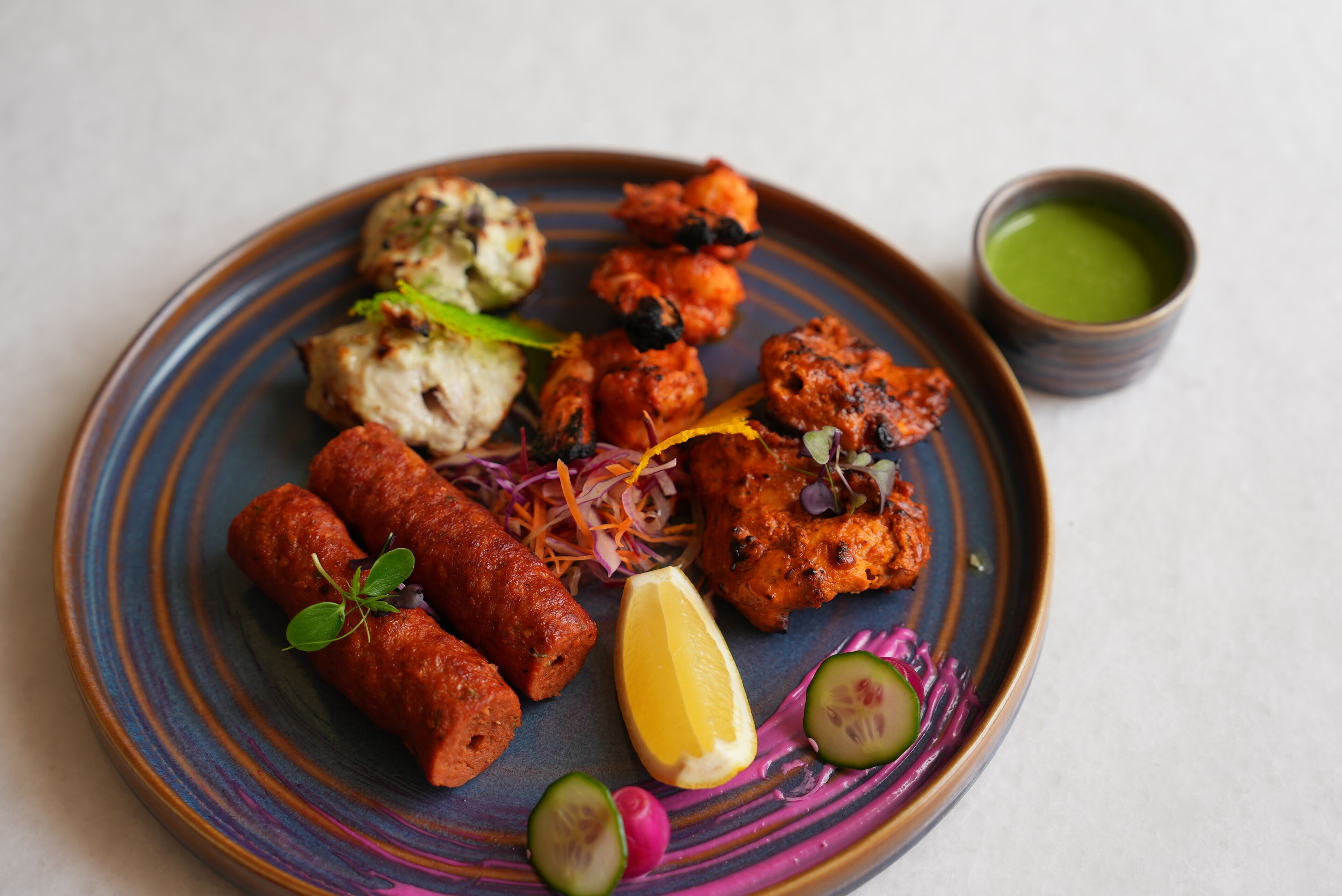 A plate of food with various items including kebabs, a piece of meat, and a bowl of green sauce.