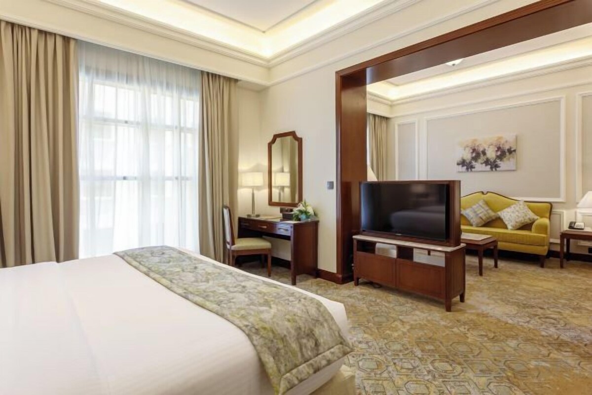 A hotel room with a large bed, a desk with a TV, a sofa, and a mirror.