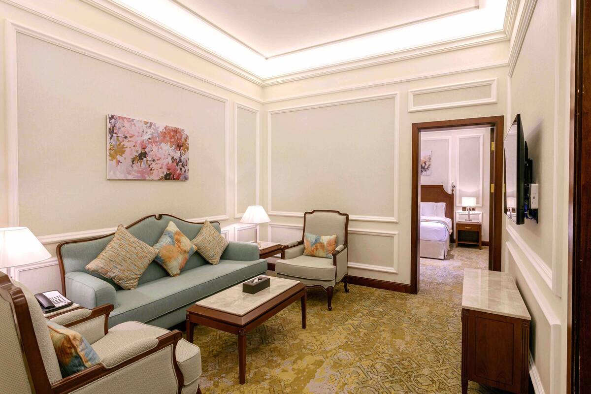 Una habitación de hotel con sofá, sillones, una mesita de centro, televisor y cama.