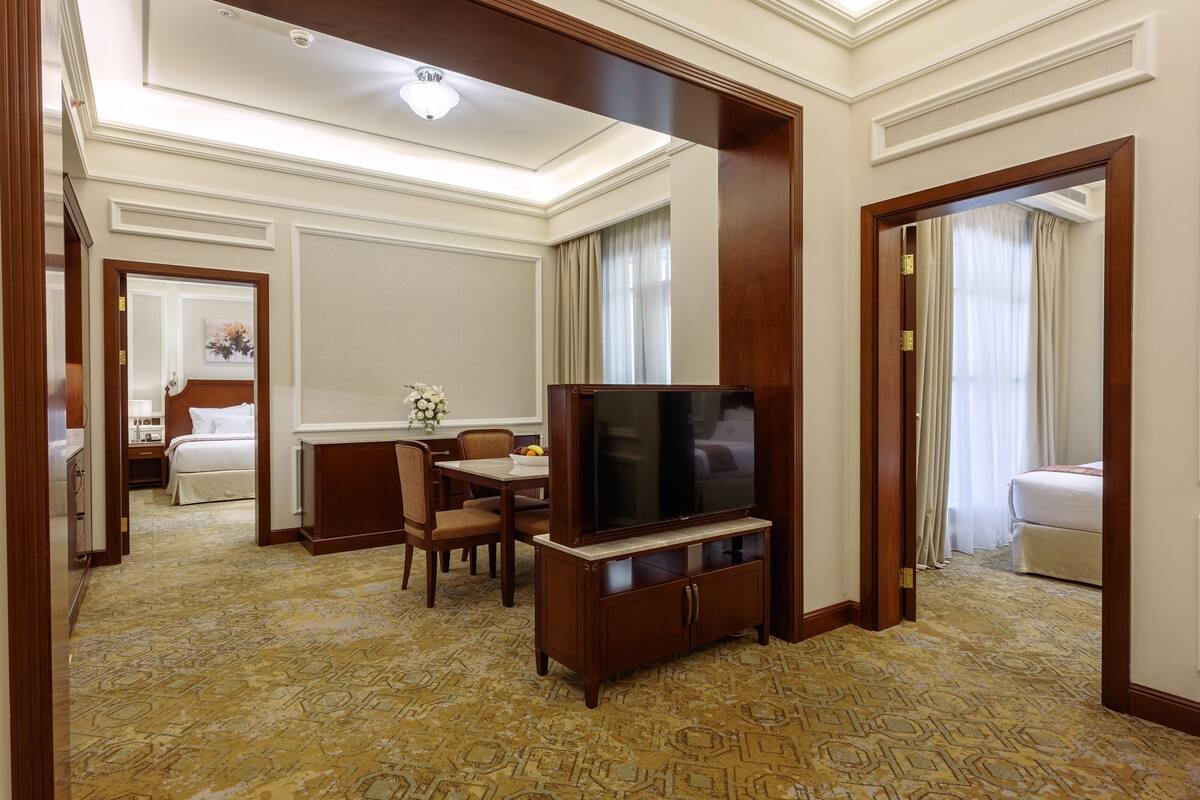 Habitación de hotel con televisión, mesa de comedor, sillas, cama y baño a la vista a través de una puerta abierta.