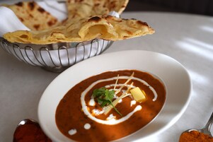 Un tazón de sopa con guarnición, un pedazo de pan plano y una cuchara.