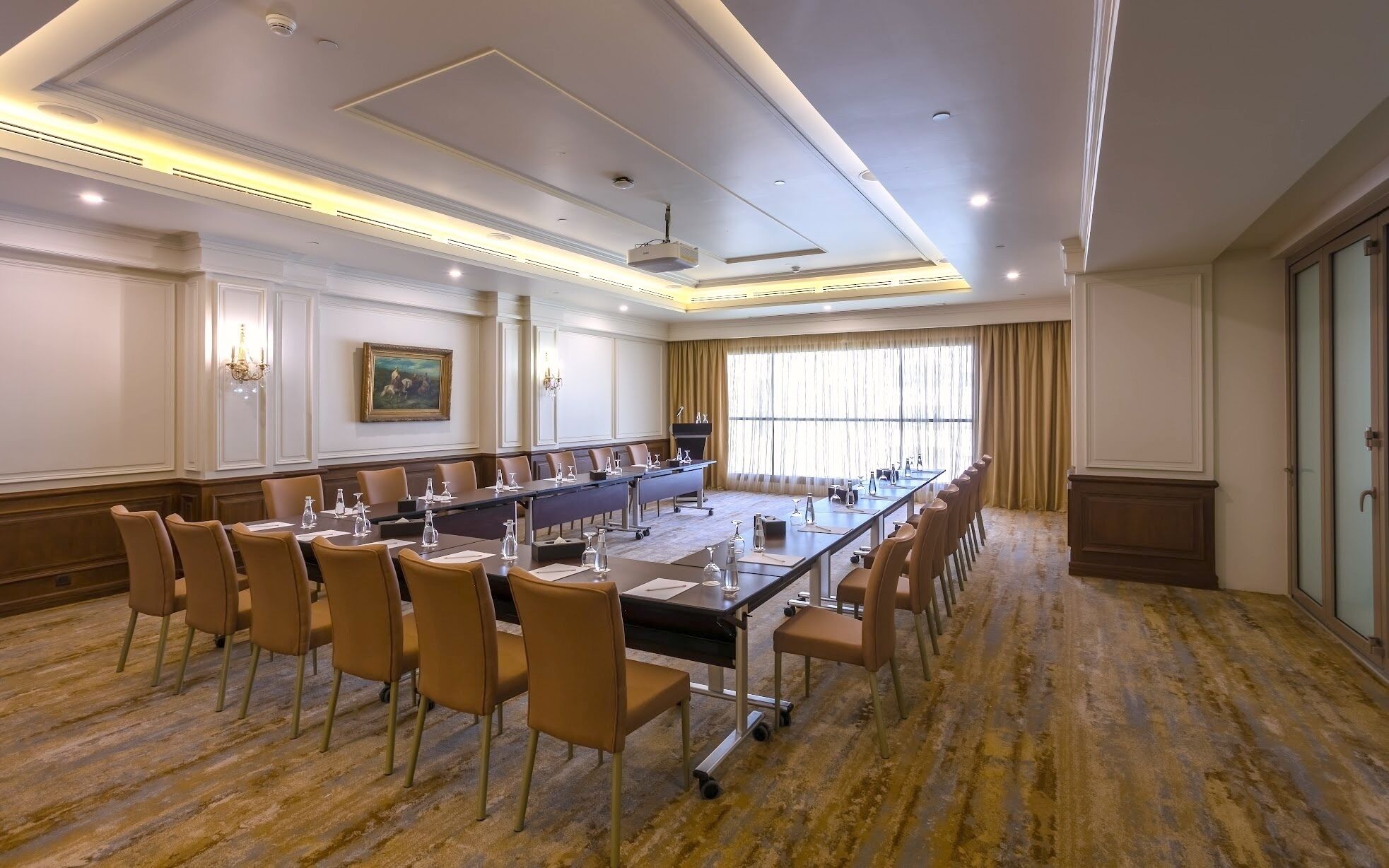 A conference room with a long table, chairs, a podium, and a painting on the wall.