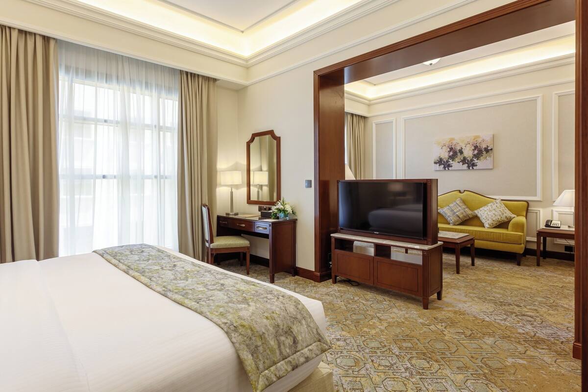 Habitación de hotel con una cama grande, un escritorio con espejo, televisor, sofá y piso alfombrado.