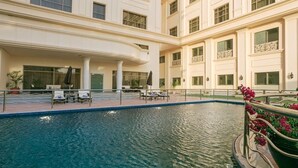 Una piscina interior con sillas de descanso y sombrillas, rodeada por un edificio con balcones y ventanas amplias.