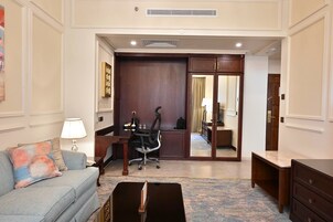 A hotel room with a sofa, a desk, a chair, a dresser, and a mirror.