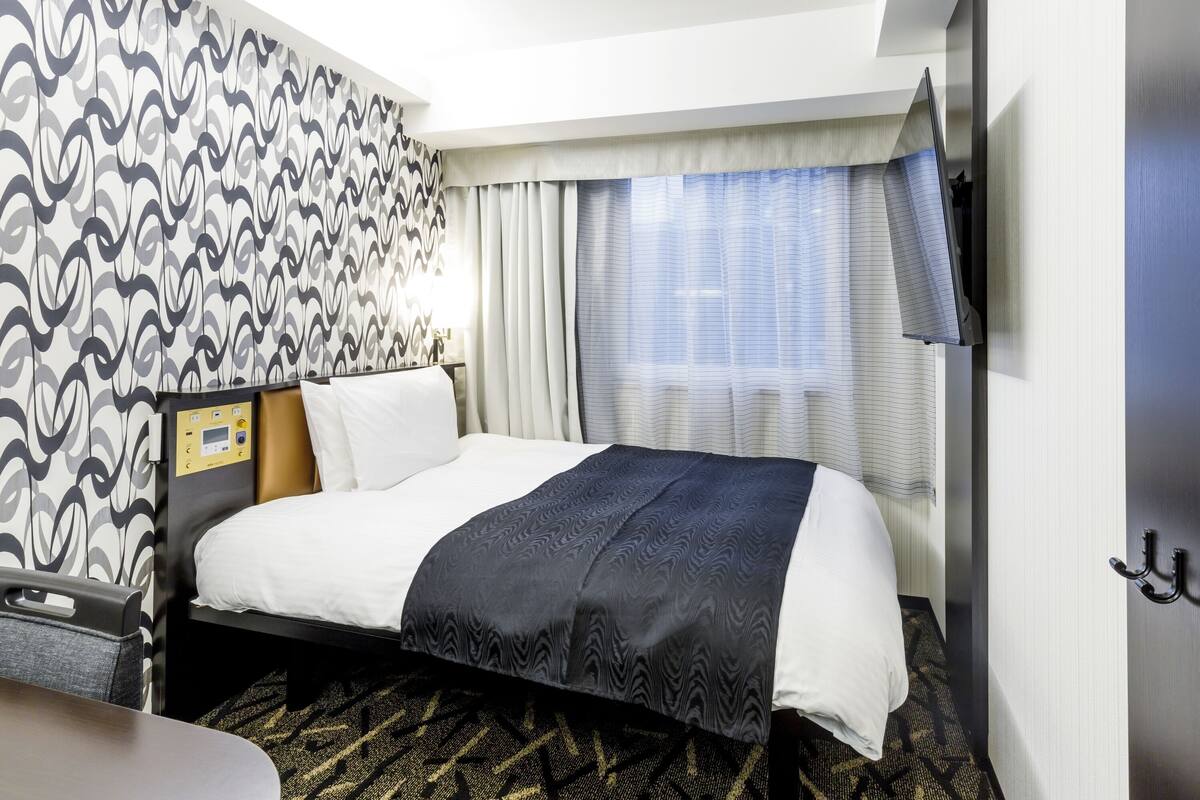 A hotel room with a bed, a control panel, a TV, and a window with curtains.