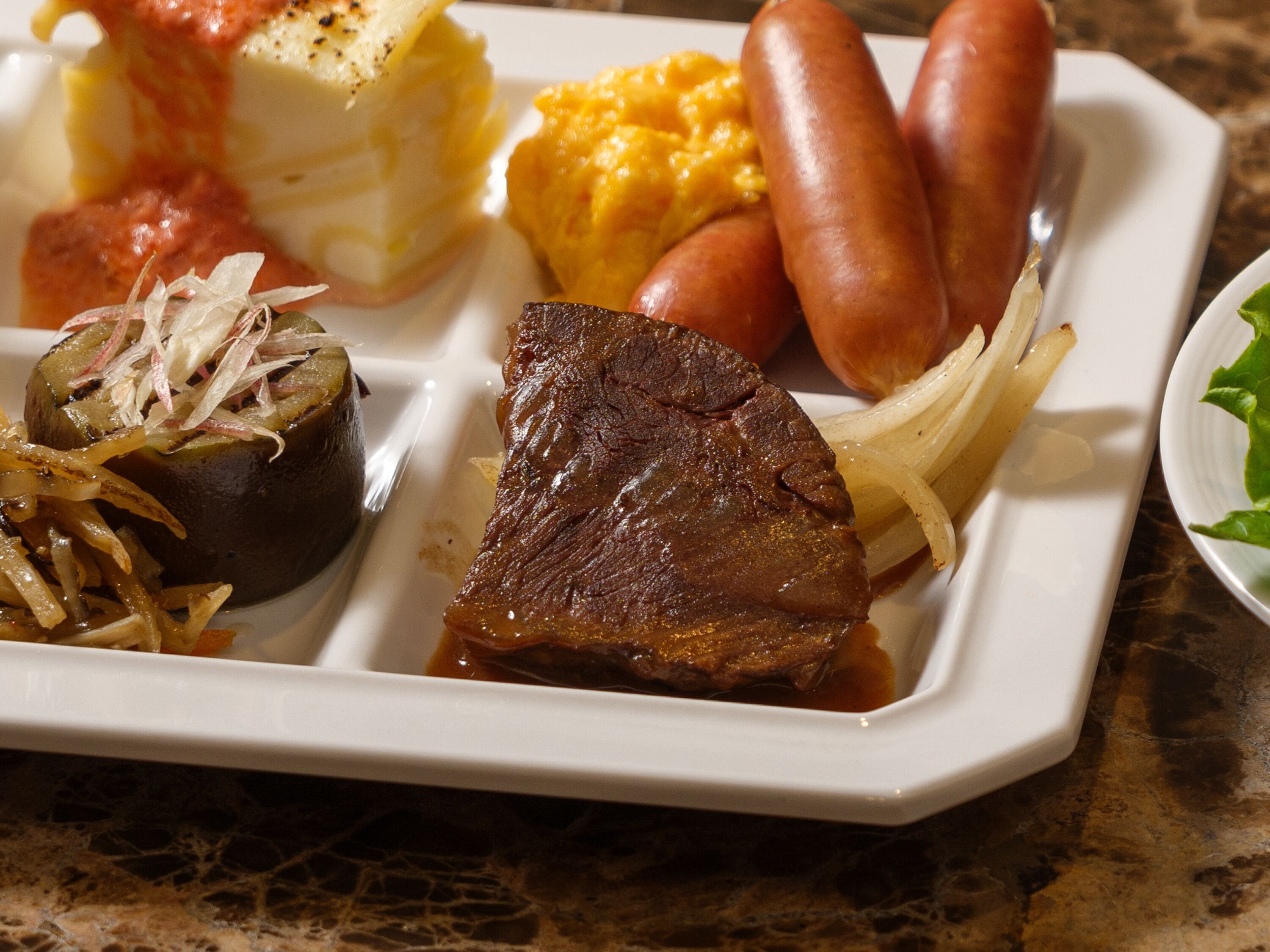 A meal with various dishes including sausages, a steak, and a baked potato.