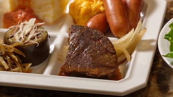 A meal with various dishes including sausages, a steak, and a baked potato.