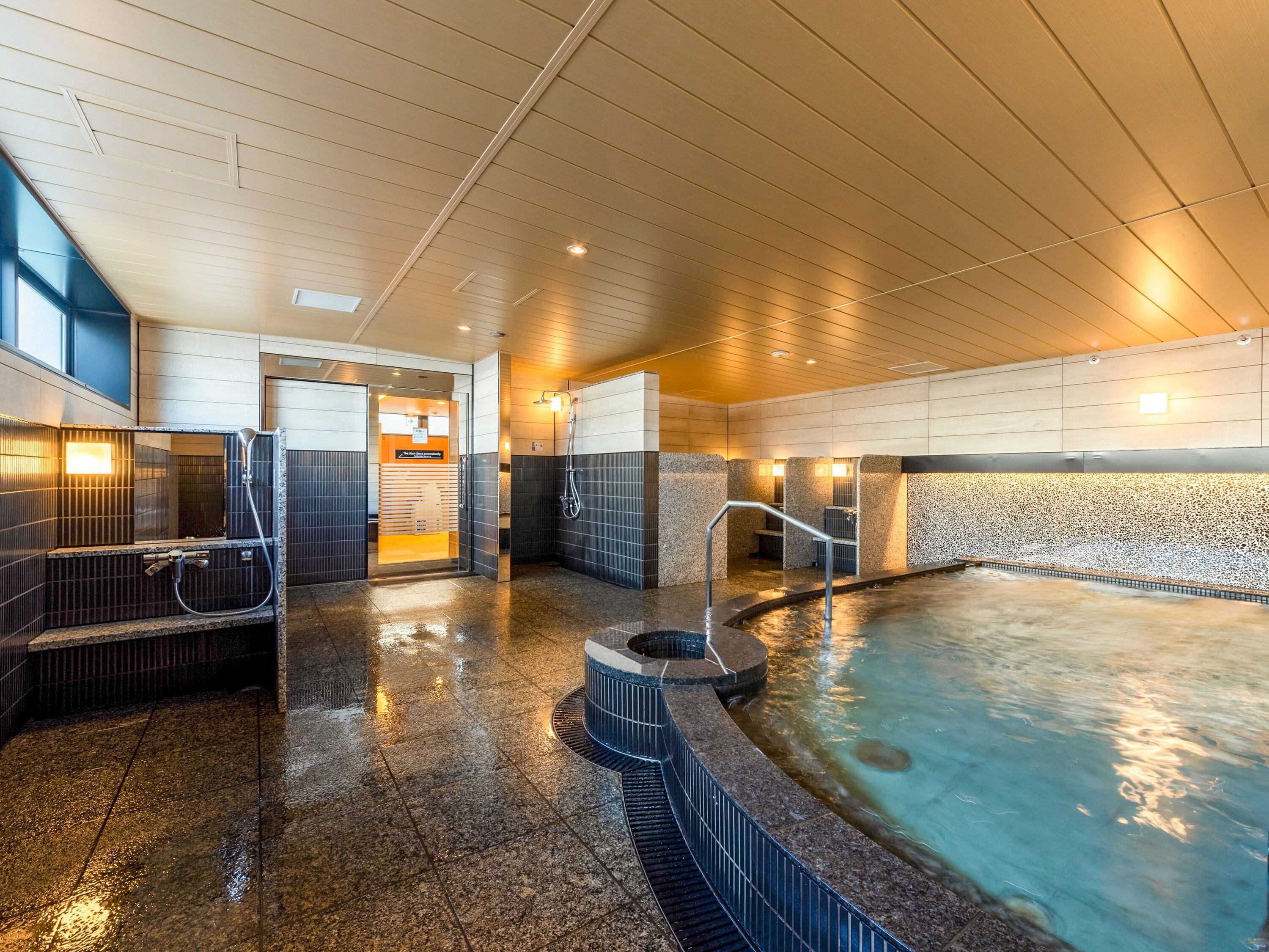 Un área de piscina interior moderna con un jacuzzi, un vestuario y zona de duchas.