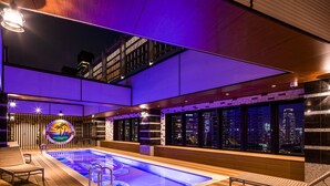 A modern indoor pool area with a city view, wooden deck, and lounge seating. - APA Hotel & Resort Roppongi Ekihigashi (Tokyo)