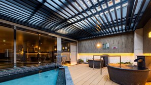 An indoor swimming pool with a wooden deck, a seating area, and a wall with a bamboo panel design. - APA Hotel & Resort Roppongi Ekihigashi (Tokyo)