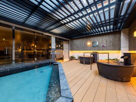 An indoor swimming pool with a wooden deck, a seating area, and a wall with a bamboo panel design.