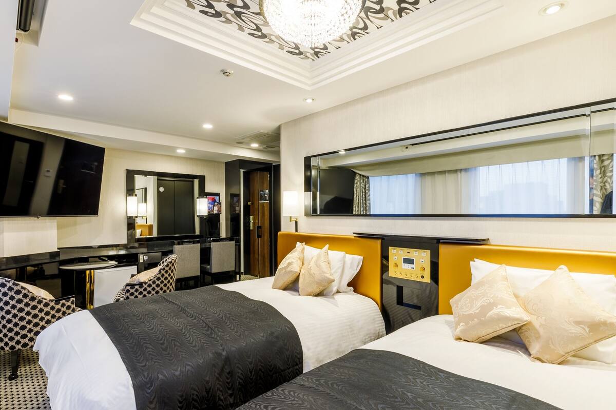 A hotel room with two beds, a desk, a chair, and a large mirror.