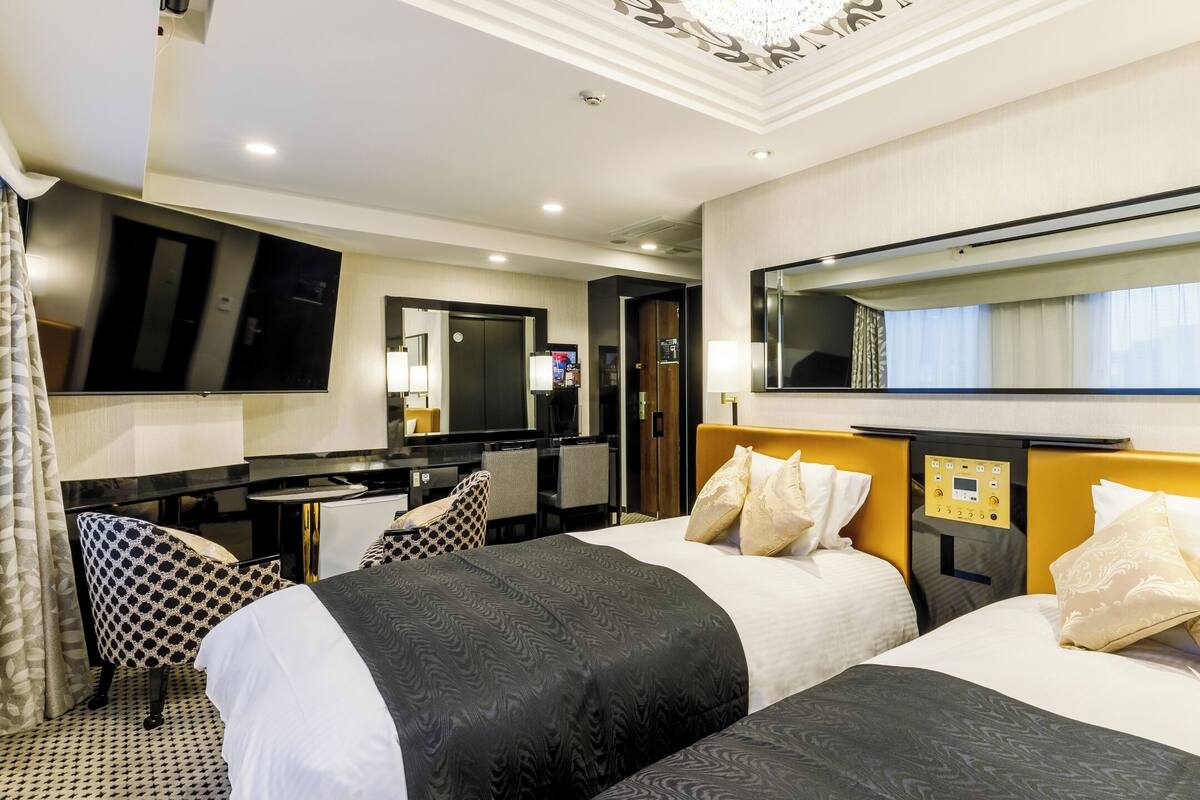 A hotel room with two beds, a desk, a mirror, and a television.
