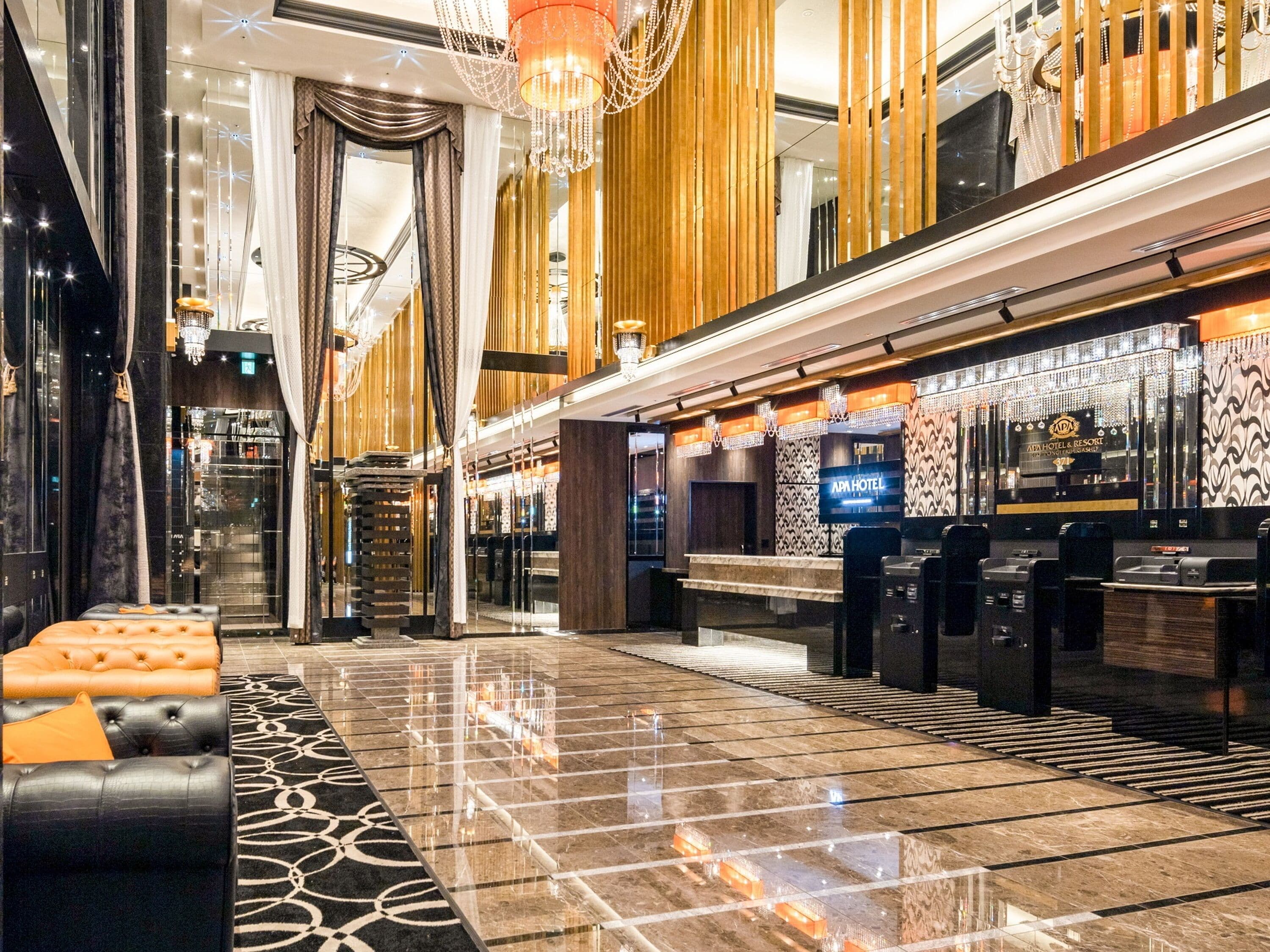 A modern hotel lobby with a check-in counter, seating area, and a staircase.