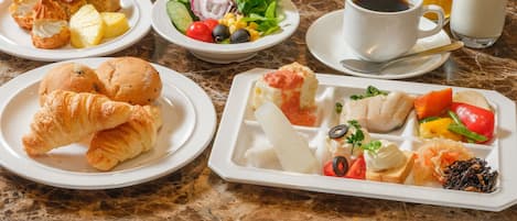 Desayuno con cruasanes, fruta y una variedad de platos sobre una mesa de mármol.