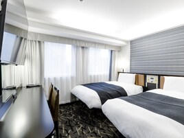 Habitación de hotel con dos camas, un escritorio, una silla, un televisor y un panel de control en la pared.