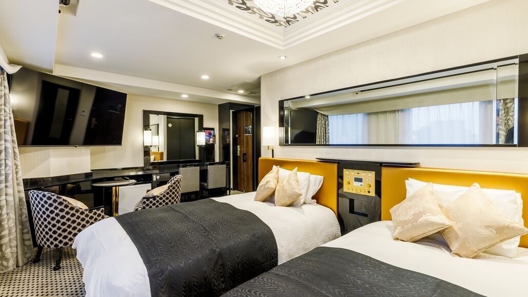 A hotel room with two beds, a desk, a mirror, and a television.