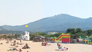 Ein Strand mit Menschen, einem Spielplatz und Bergen im Hintergrund.