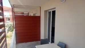 Ein Balkon mit einer roten Trennwand, einem weißen Tisch und zwei blauen Stühlen.
