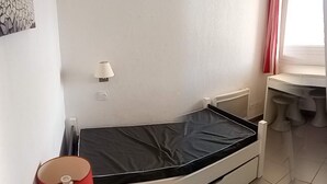 Ein kleiner, kompakter Raum mit einem Einzelbett, einem Nachttisch, einer Lampe und einem fenster mit Vorhängen.