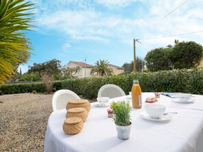 An outdoor dining area with a table set for two, featuring woven baskets, a potted plant, and a bottle of orange juice.