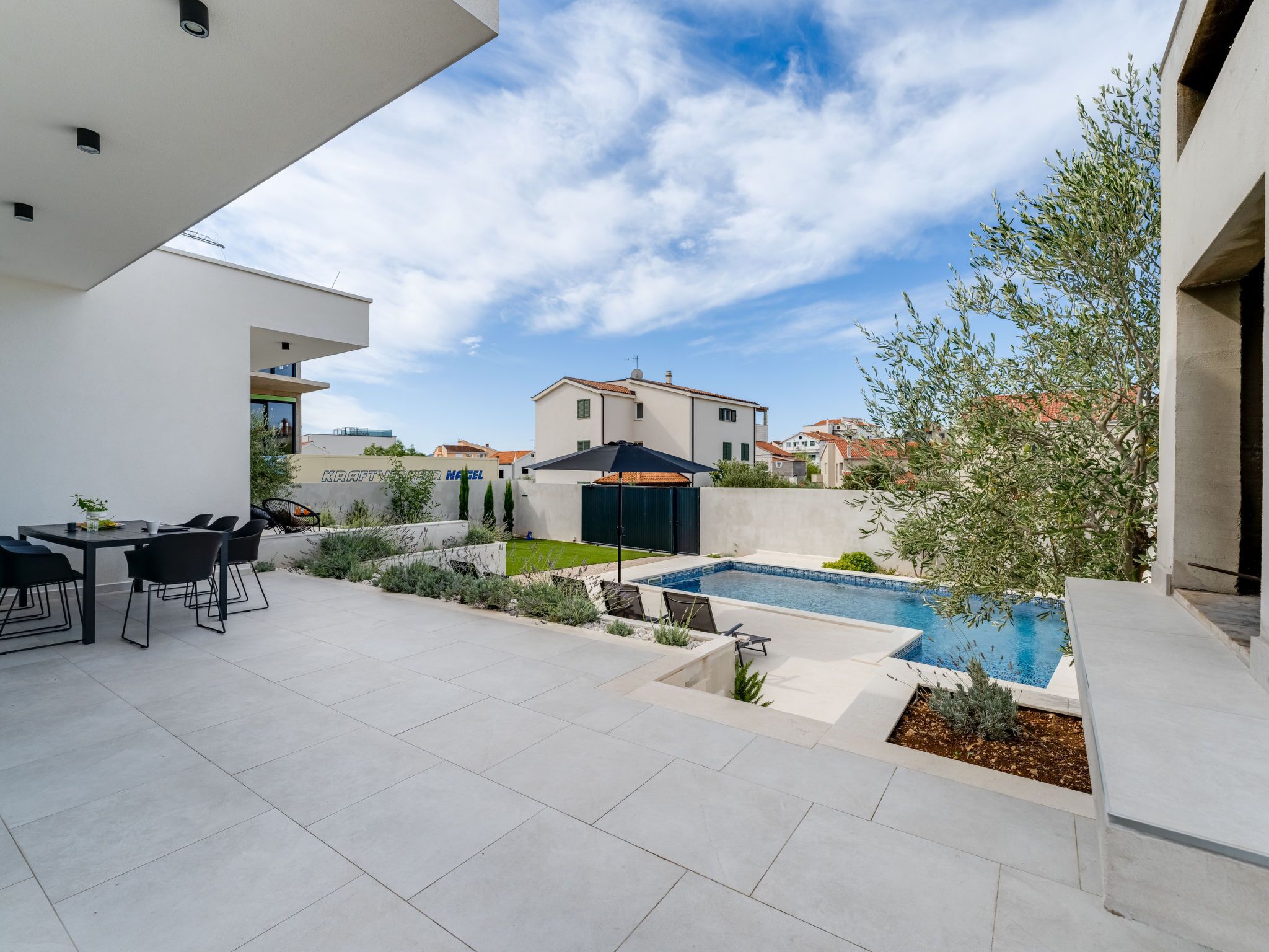 A modern outdoor patio with a pool, seating area, and a view of neighboring houses.