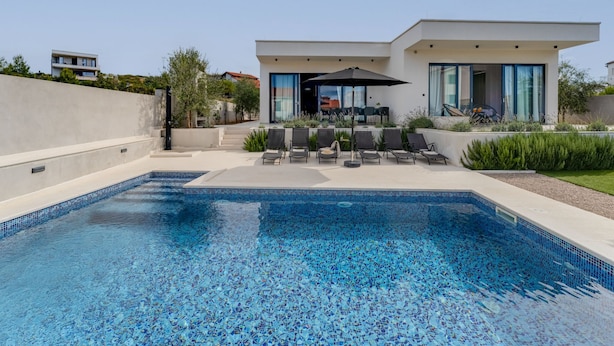 A modern pool area with a clear blue pool, lounge chairs, and a patio with a table and umbrella. - Vacation home Inizio by Interhome (Brodarica)