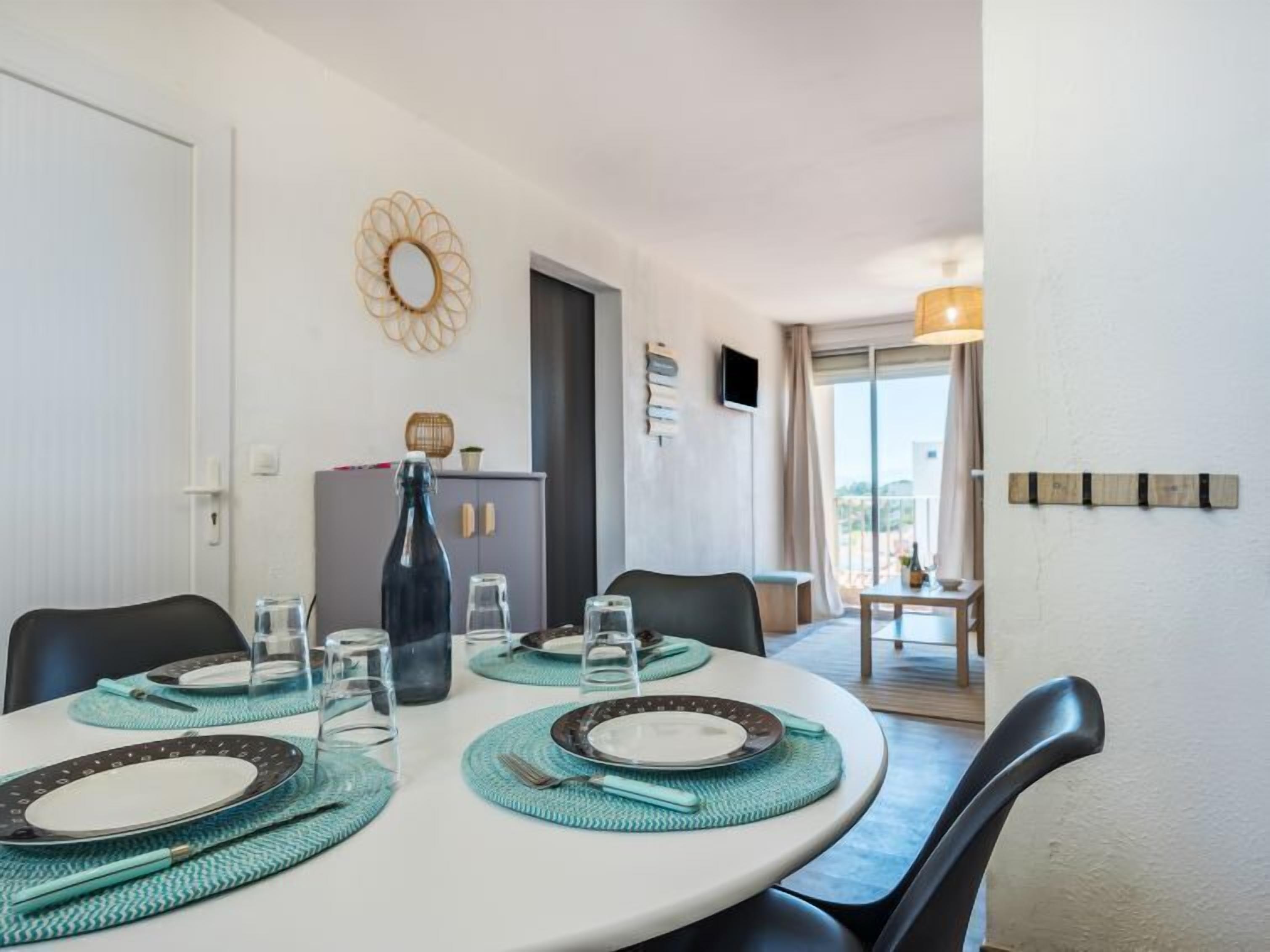 A dining area with a round table set for four, a cabinet with decorative items, and a view through a glass door.