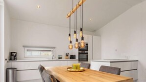 Une cuisine moderne avec une table à manger en bois, des chaises à revêtement gris et des luminaires suspendus.