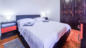 Una cama bien hecha con ropa blanca, una mesita de noche con lámpara y un armario de madera con diseños elaborados.