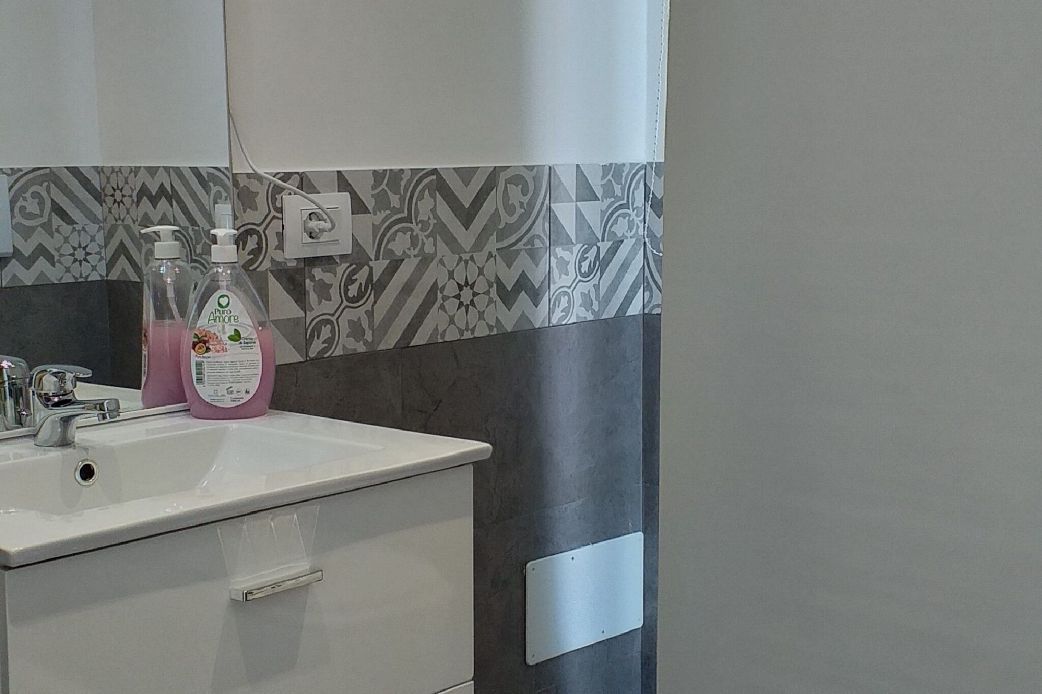A bathroom with a white sink, a mirror, and patterned tiles on the wall.