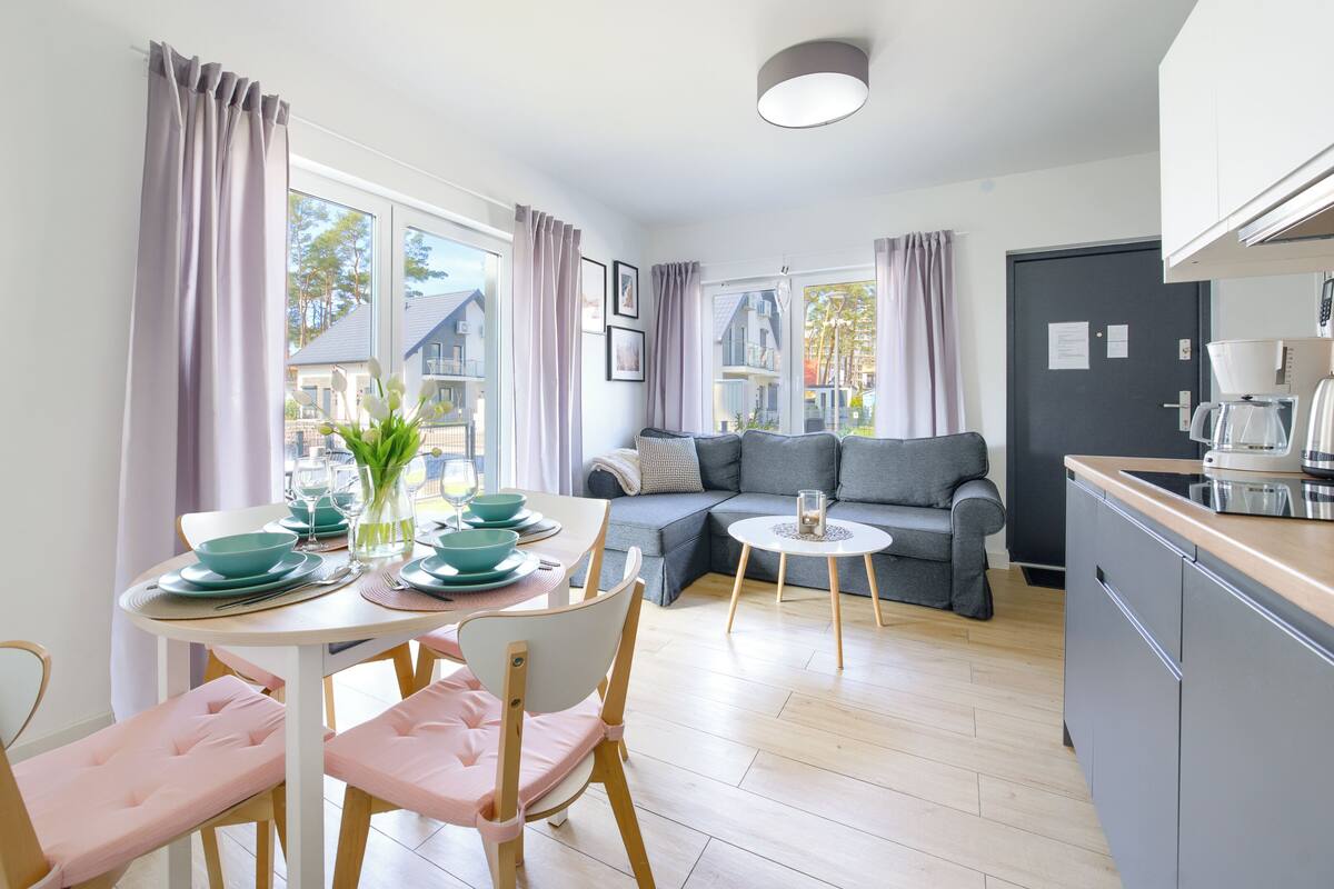 A modern kitchen with a coffee maker, a kettle, and a dining area with a table set for four.