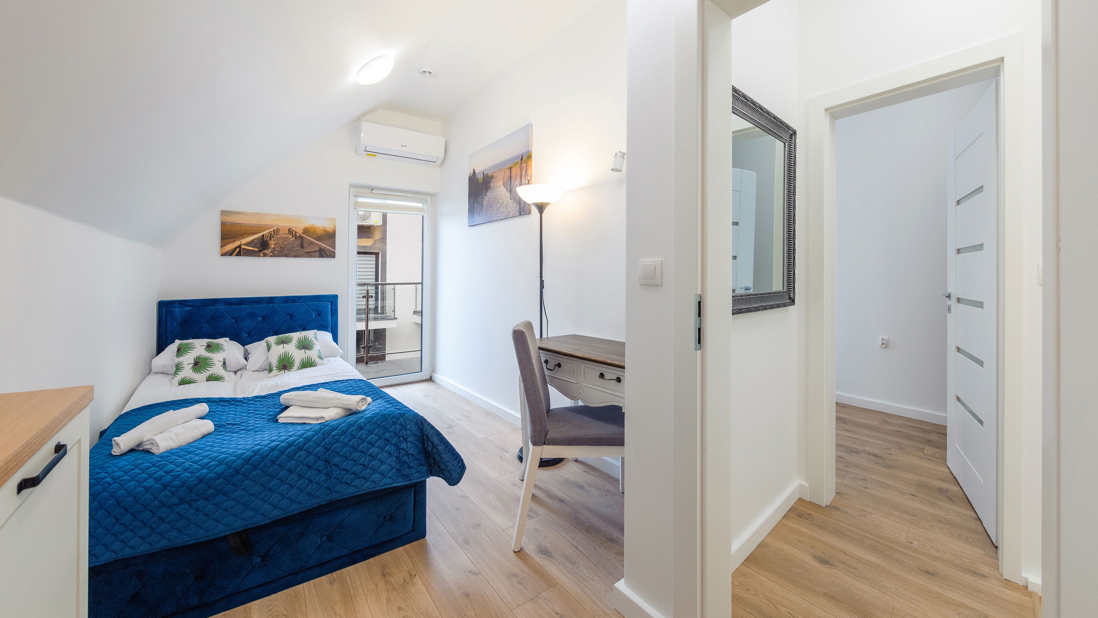 Una camera da letto con un letto blu, una scrivania e una porta che dà su un'altra stanza.