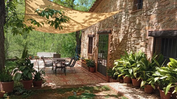 A patio with a table and chairs, surrounded by potted plants and a stone wall.