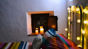 A bed with colorful bedding, a small window with candles, and a wall with decorative lights.